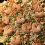 shrimp fried rice meme recipe in a black wok with peas, carrots, and fluffy scrambled eggs