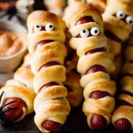 Mummy Pigs in a Blanket hot dogs with candy eyes and dipping sauce